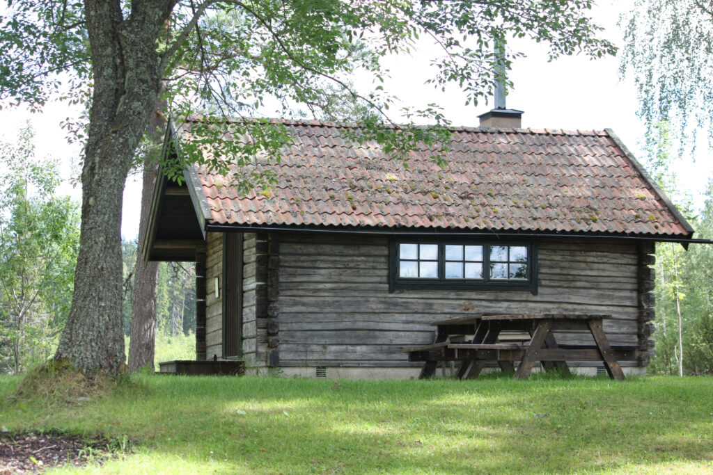 En grå timmerstuga med ett picknickbord framför.